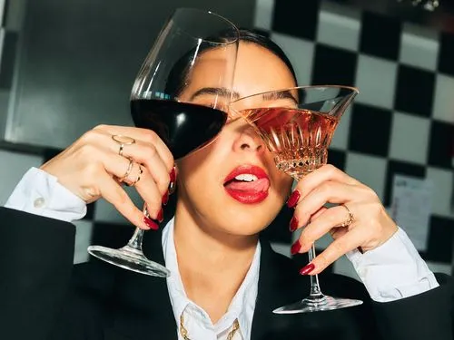 Person holding a glass of red wine and a glass of rosé wine close to their face, with red lipstick and manicured nails.