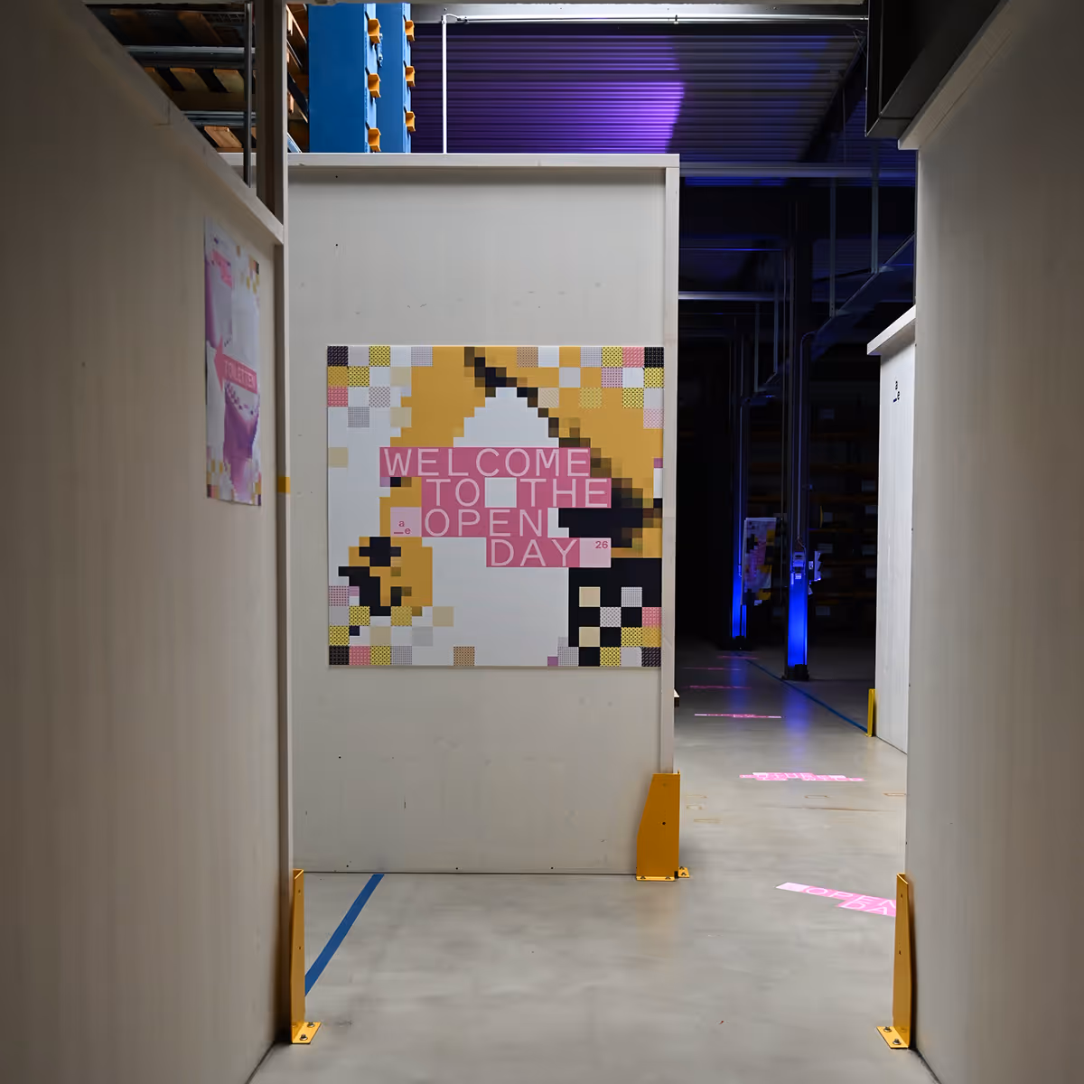 Warehouse aisle with a pixelated sign saying Welcome to the Open Day in pink and yellow tones.