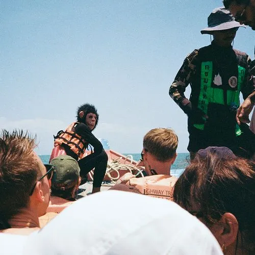 Group of people on a boat with a person wearing a monkey mask and life jacket, and a crew member in a green and black uniform.