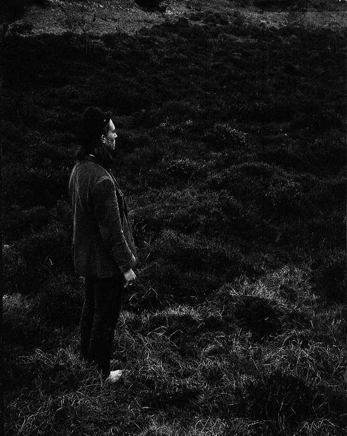Black and white photo of a man standing barefoot on grass, looking to the left.