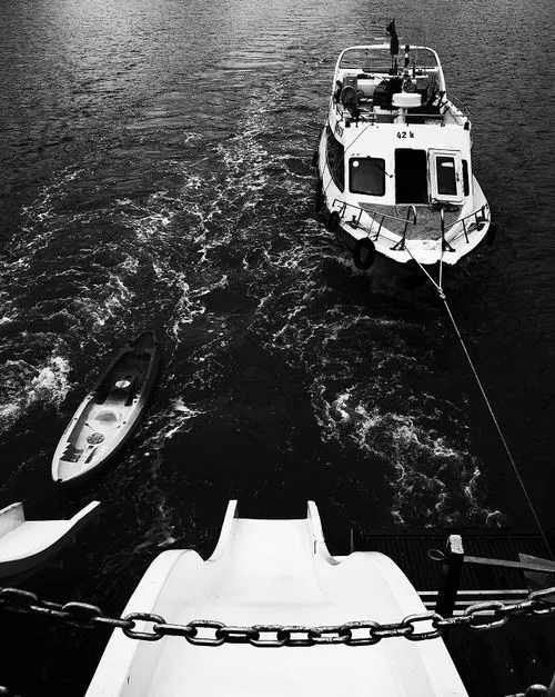 Black and white photo of a boat named '42 k' anchored on water viewed from above near a waterslide with a kayak floating nearby.