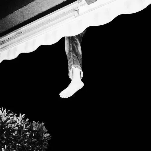 A bare foot and lower leg in jeans hanging from a white awning against a black sky at night.