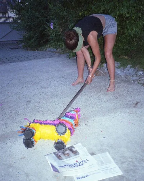 Person blindfolded holding a stick, preparing to hit a colorful donkey-shaped piñata on the ground.