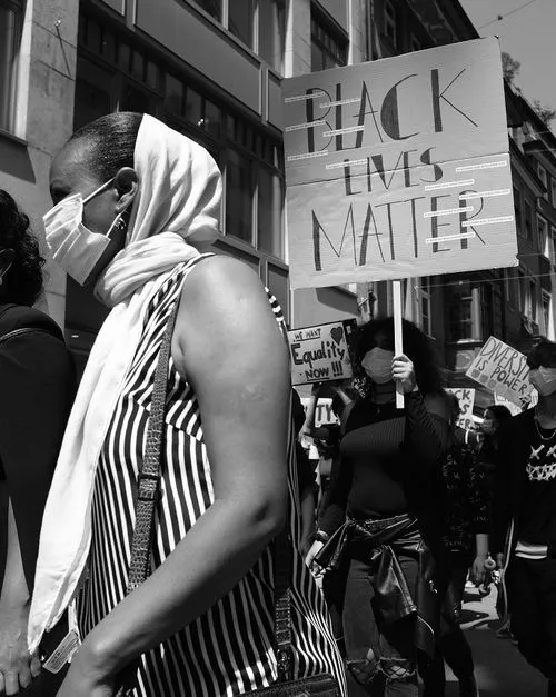 Black and white photo of a protest with people wearing face masks, one holding a 'Black Lives Matter' sign.
