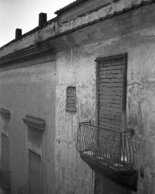 Black and white photo of an old building with a small balcony and door sealed with bricks.