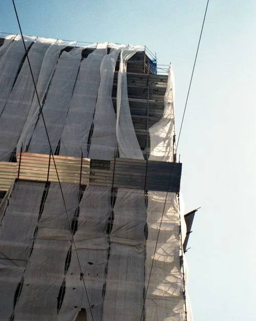 Building under construction covered with white protective sheeting and metal scaffolding, against a clear blue sky.
