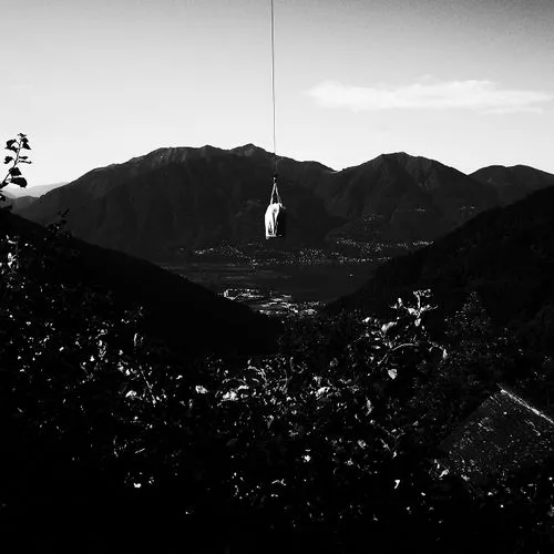 Cargo delivery by helicopter above a valley with mountains in the background.